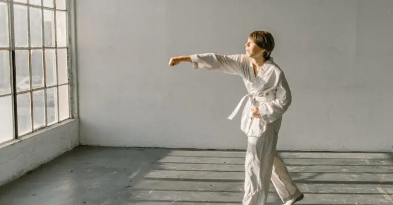 A young boy in a white martial arts uniform throwing a punch in a bright, sunlit studio, showcasing basic moves for a beginner self defense training guide.
